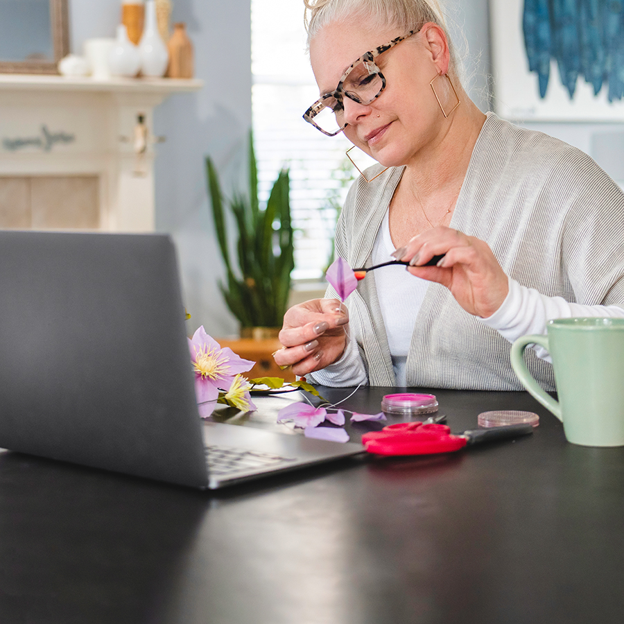 A woman making paper flowers in front of a laptop.