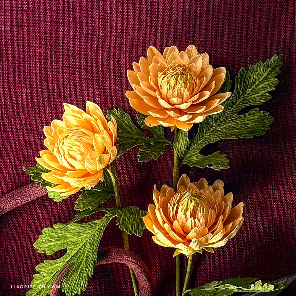 Small golden yellow crepe paper chrysanthemum blooms with green leaves